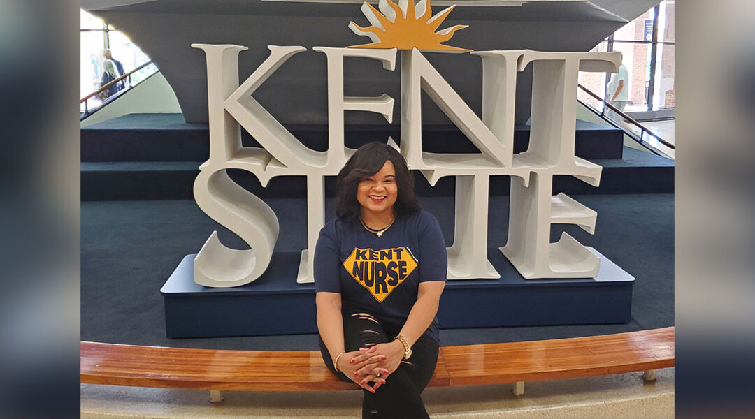 Alumna Shenell Hinton, MSN, BSN ‘95, RN, CRRN, CCM, sits by the Kent State logo display in the Kent Student Center lobby.