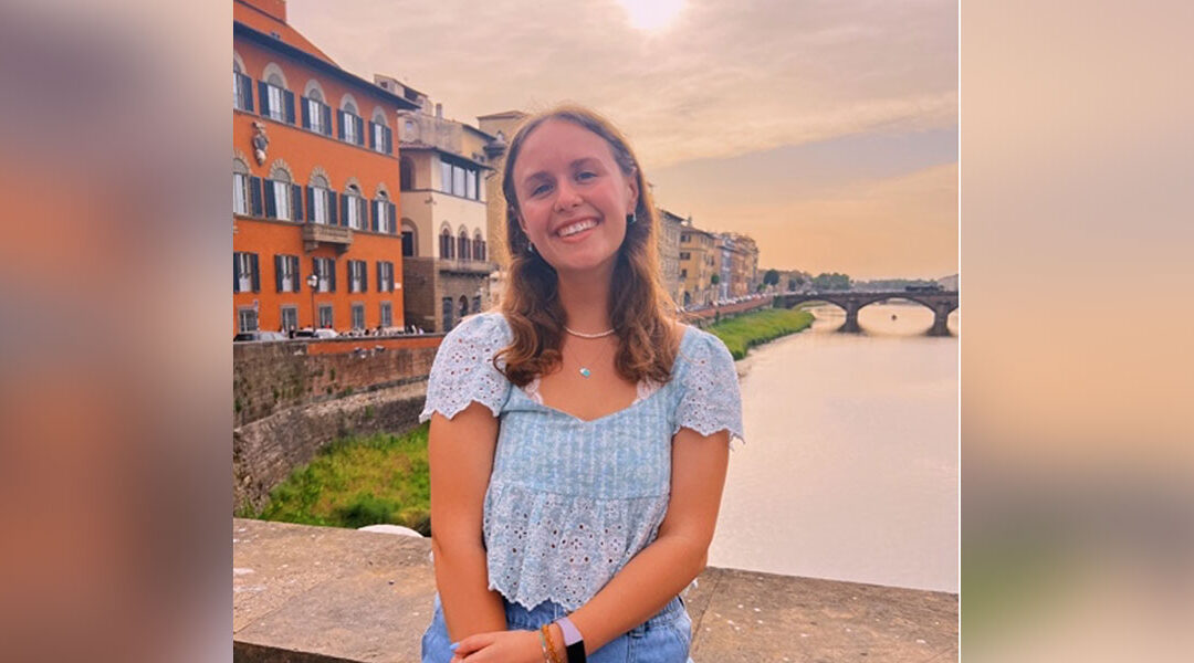Taylor Kristufek poses on a bridge in Italy over a river.