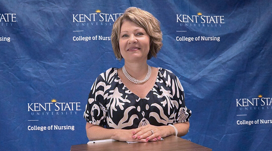 Michelle Michel poses in front of the Kent State College of Nursing branded backdrop prior to giving her research presentation.