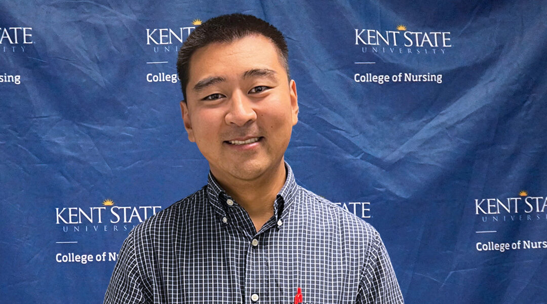 Wayne Nieh, BSN, poses for a photo in front of the Kent State University College of Nursing branded backdrop prior to his presentation.