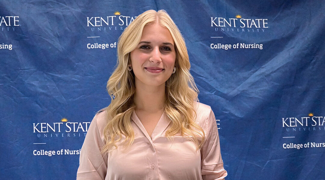 Katie Murray stands in front of the Kent State University College of Nursing branded backdrop before giving her presentation.