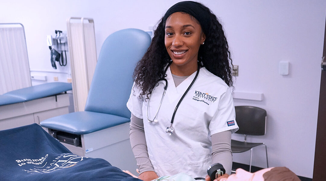 Destiny Nash, wearing her Kent State nursing scrubs, poses for a photo near one of the manikins in the skills lab.